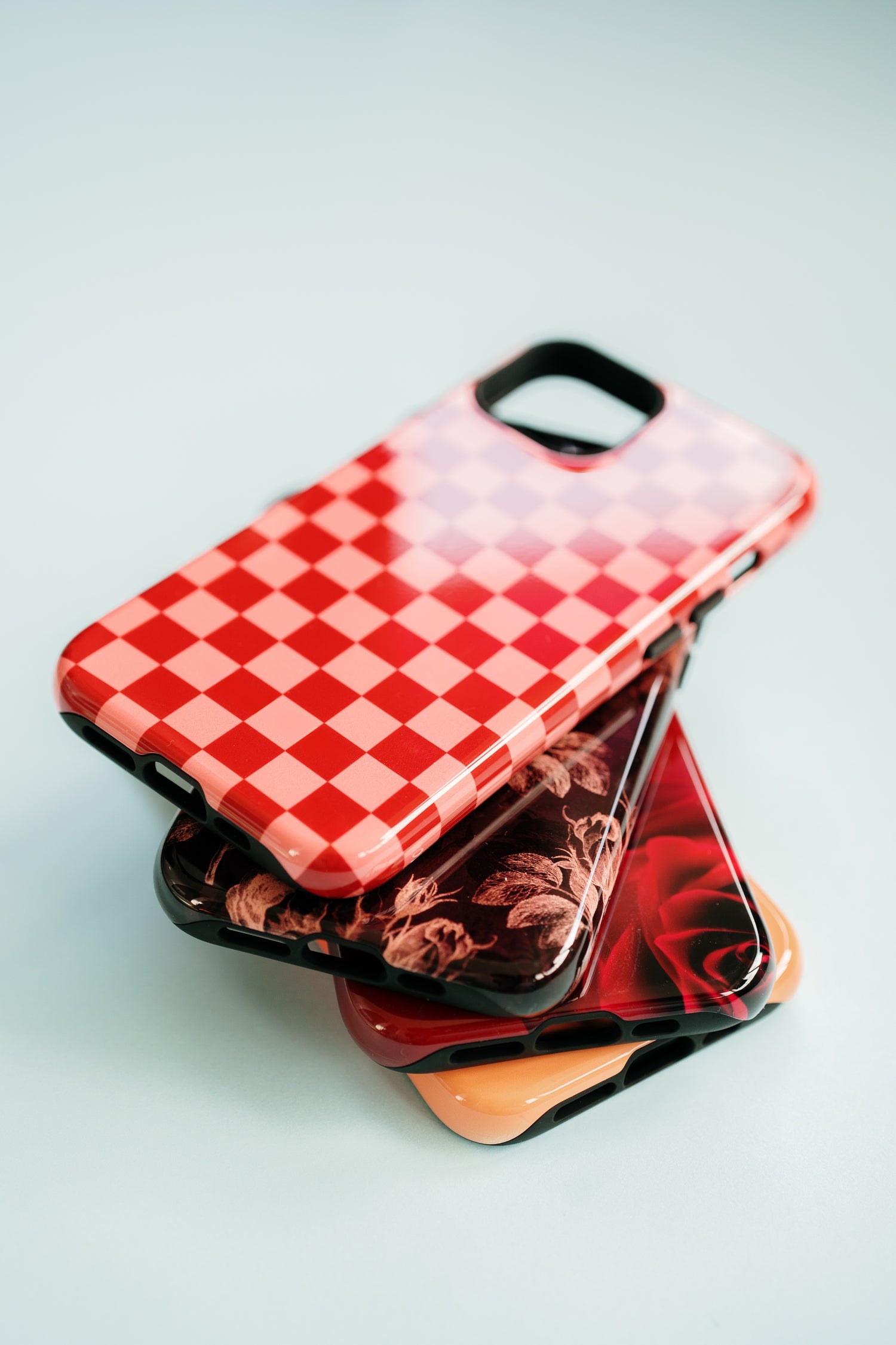 Stack of high fashion phone cases from Depiction Phone Cases featuring red checkerboard iphone case, floral iphone case, and rose iphone case - stylish protective phone cases for iPhone, Samsung Galaxy, and Google Pixel
