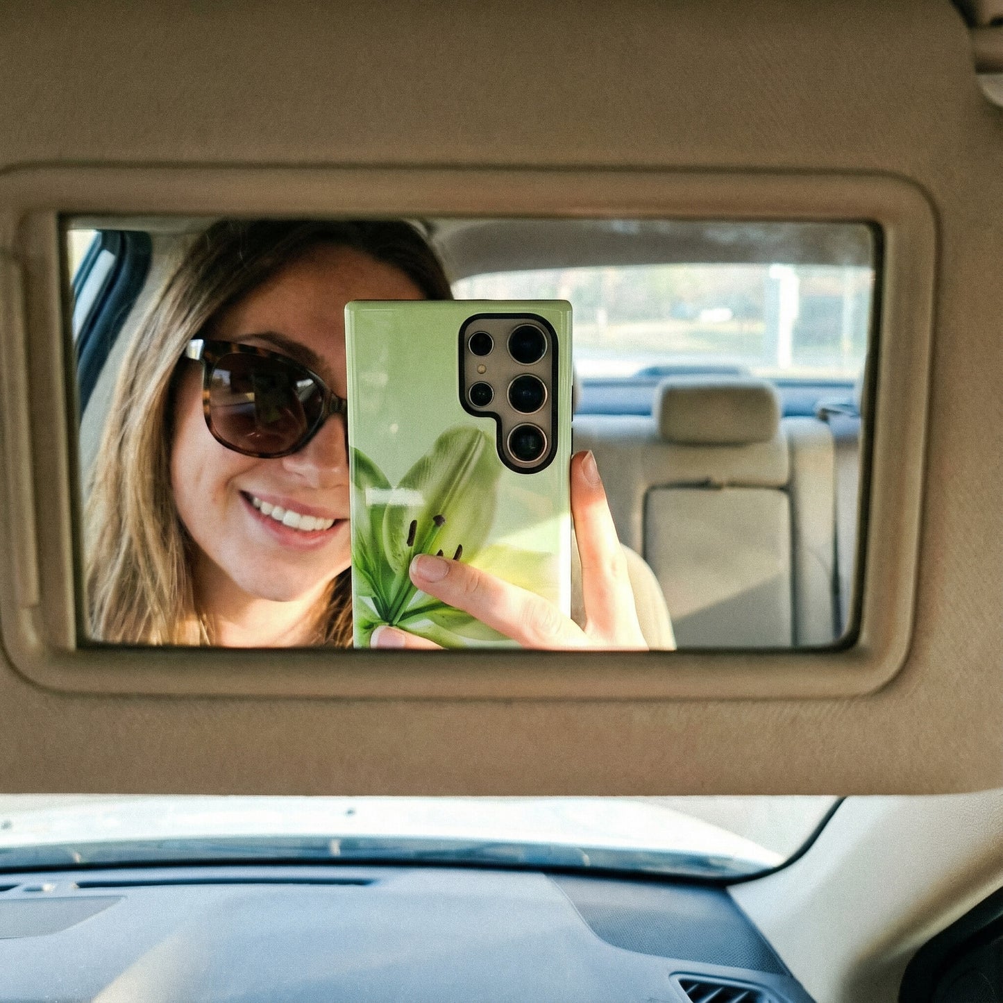 Woman taking a selfie in a car's rearview mirror with a samsung galaxy S24 ultra with a floral green phone case.