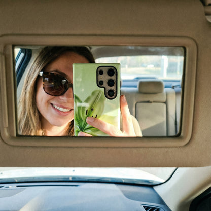 Woman taking a selfie in a car's rearview mirror with a samsung galaxy S24 ultra with a floral green phone case.