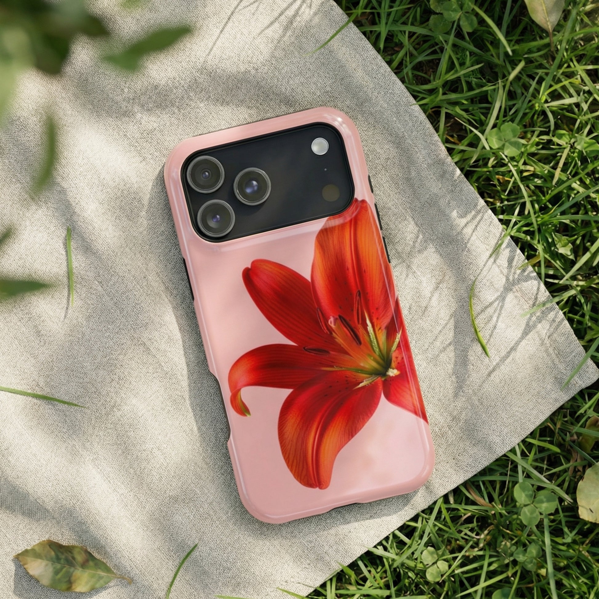 iPhone 17 pro max case with a red flower design sitting on a fabric surface with a grass background