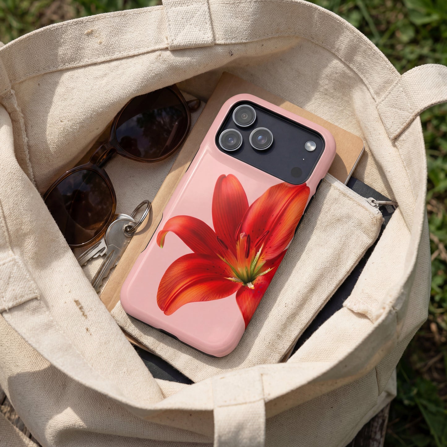 iPhone 17 pro max case with red flower design in a beige tote bag with sunglasses and keys.