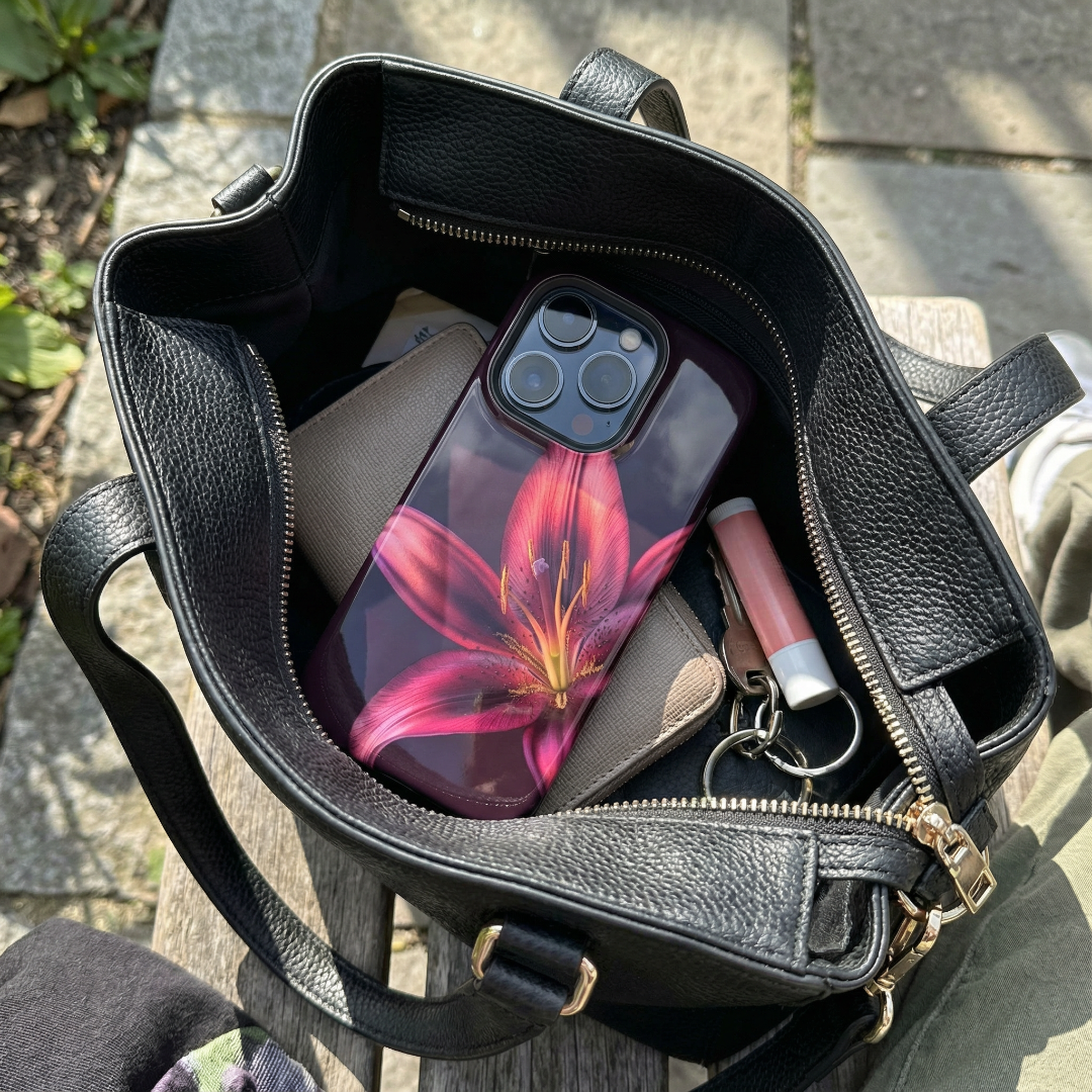 Black handbag with a Floral iphone case, wallet, and keys on a stone surface