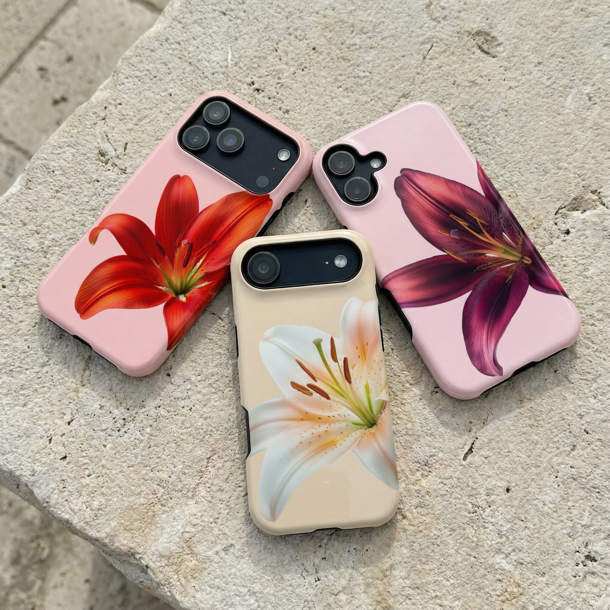 Three iphone cases with floral designs sitting on a stone surface