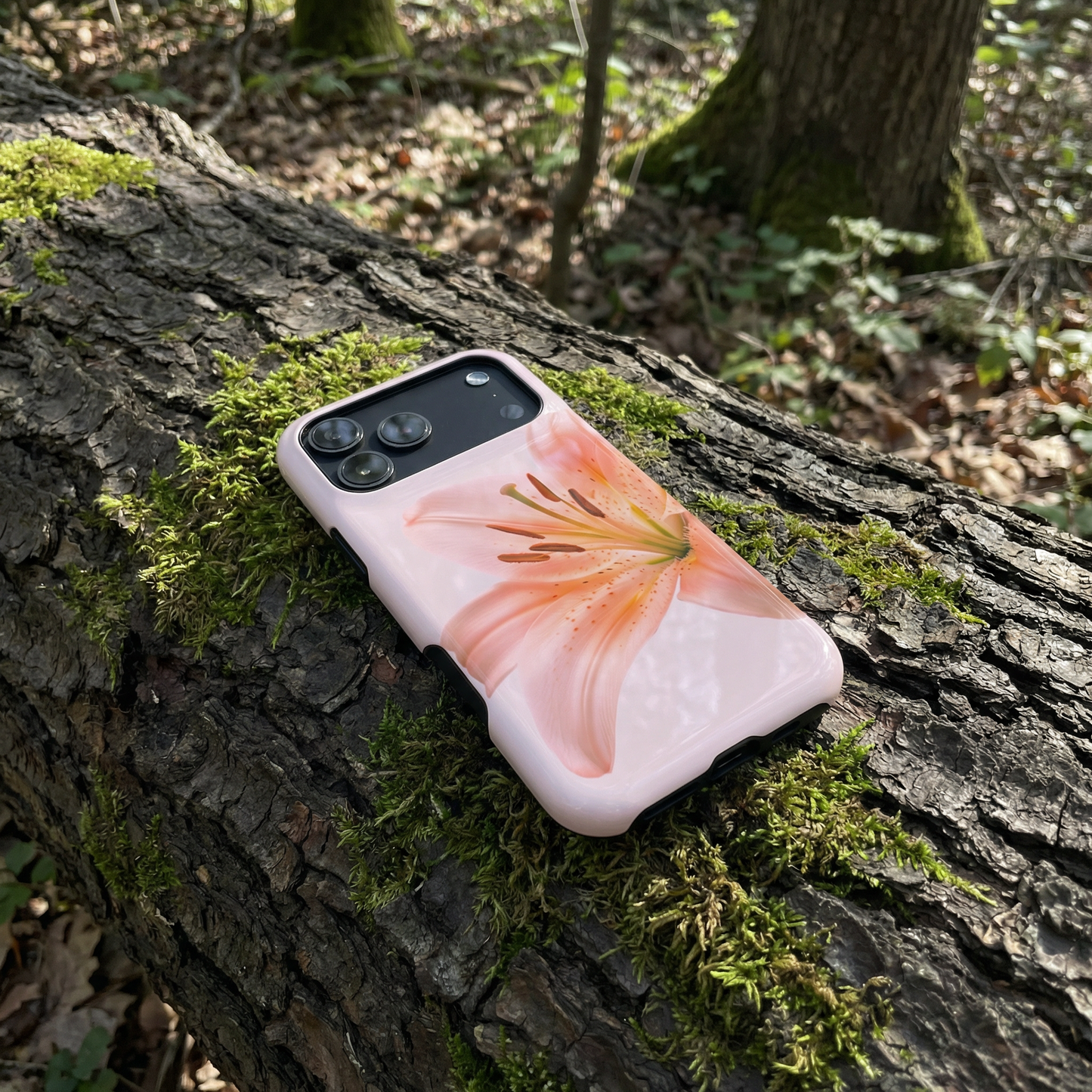 iPhone 17 pro max case with a pink floral design sitting on a tree trunk in a forest setting