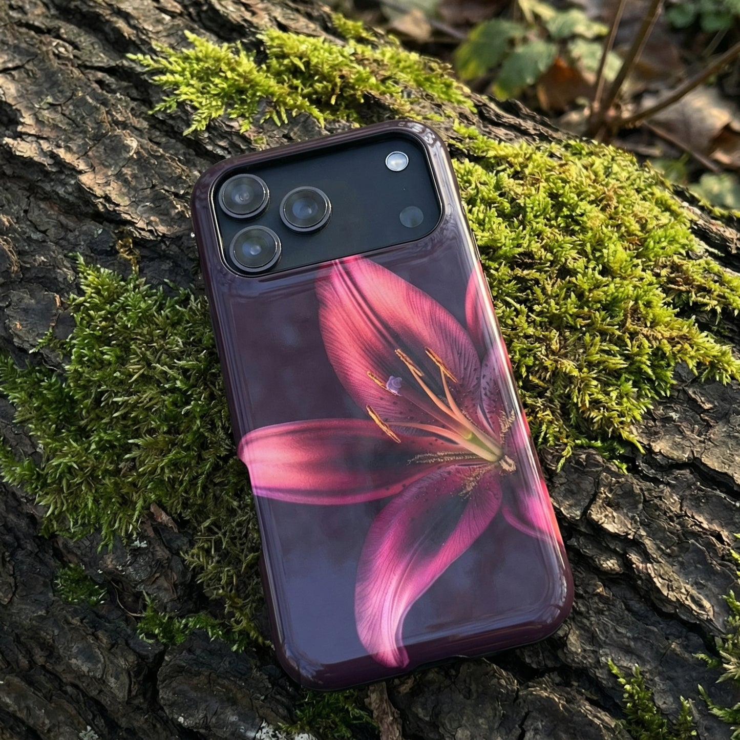 iPhone 17 pro max case with a purple floral design sitting on a mossy tree trunk