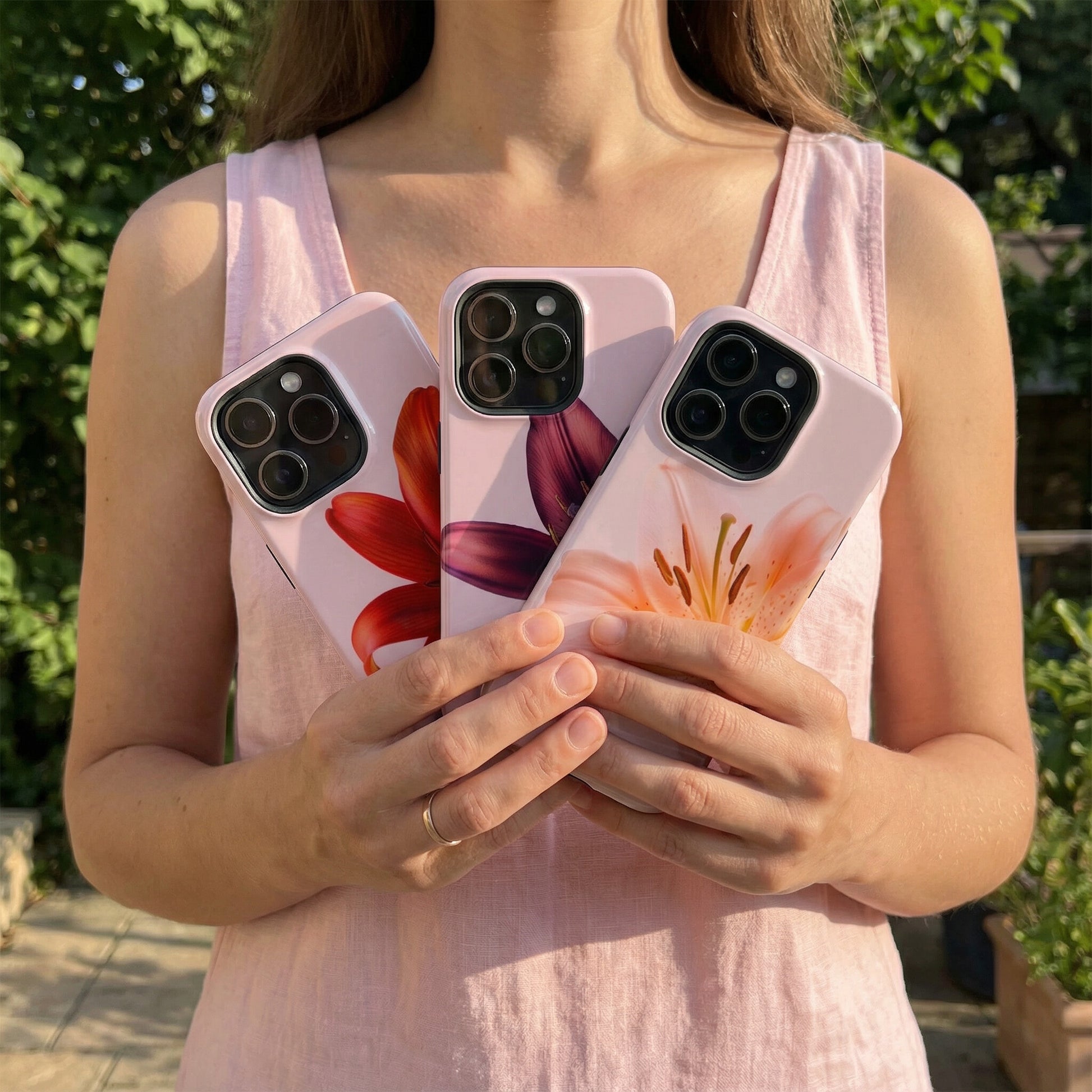 Woman holding three floral iphone cases in front of a blurred garden background