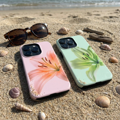 Two iphone cases with floral designs on a sandy beach with sunglasses and shells.