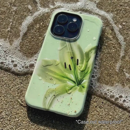 Green iPhone case with floral design sitting on beach sand as waves gentle wash over it.