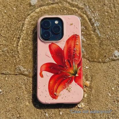 pink iPhone case with red floral design sitting on beach sand as waves gentle wash over it.