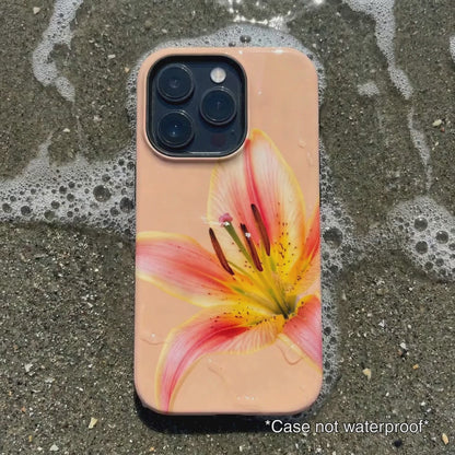 orange iPhone case with pink floral design sitting on beach sand as waves gentle wash over it.