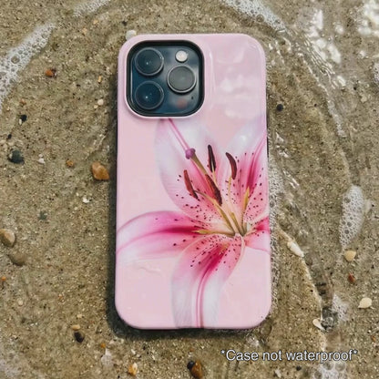 pink iPhone case with floral design sitting on beach sand as waves gentle wash over it.